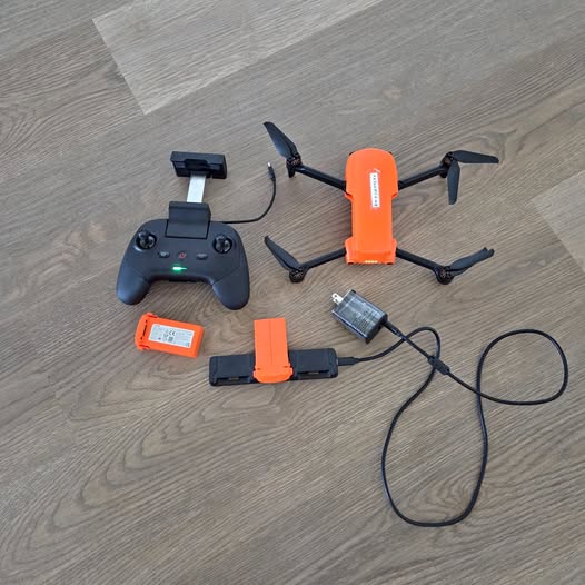 Orange drone with black remote controller, battery, and charging cable set