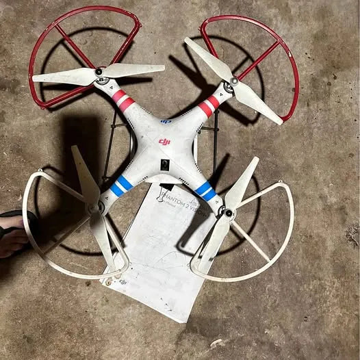 White quadcopter drone with four propellers, red guards, and blue striped accents