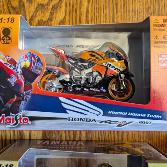 Diecast motorcycle model in retail box, orange and black racing bike with Repsol Honda graphics
