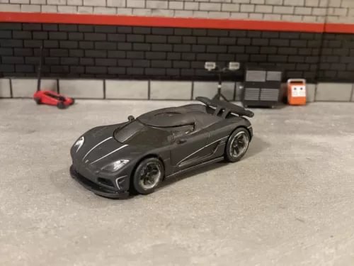 Weathered 1/64 scale diecast sports car, dark gray, front 3/4 view