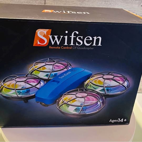 Blue quadcopter drone with four propeller guards shown on retail box packaging.