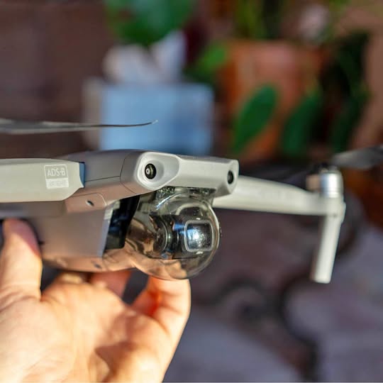 Drone with front camera and gray/white body, held in hand.