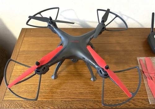 Grey and red quadcopter video drone with four propellers and landing legs