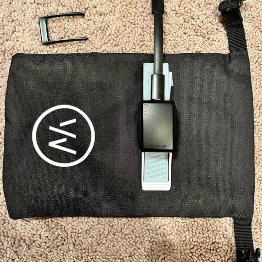Black pouch with circular logo, strap, and attached fitness tracker module
