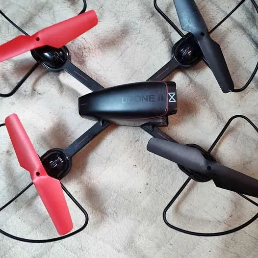 Quadcopter drone with black body, red arms, and four propellers