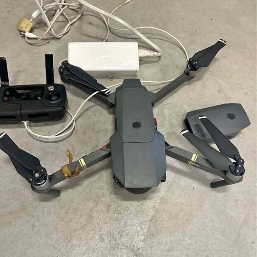 Gray quadcopter drone with foldable arms and prop guards, plus remote controller and battery pack