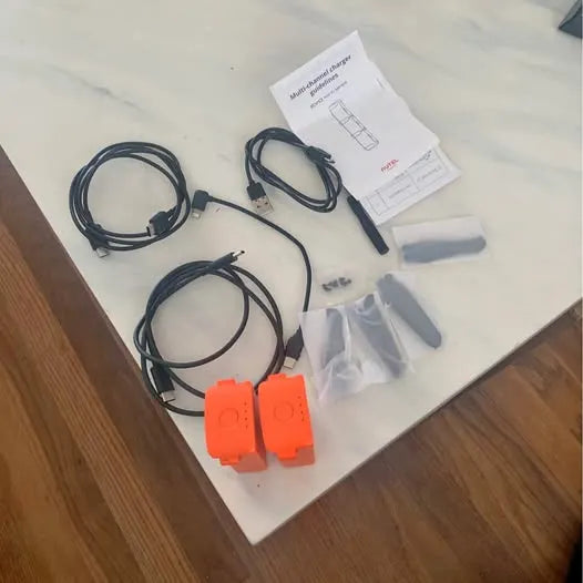 Drone accessories with orange battery modules, black cables, and instruction booklet