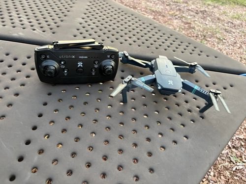 Quadcopter drone with black remote controller and gray-blue body, visible propellers