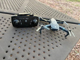 Quadcopter drone with black remote controller and gray-blue body, visible propellers