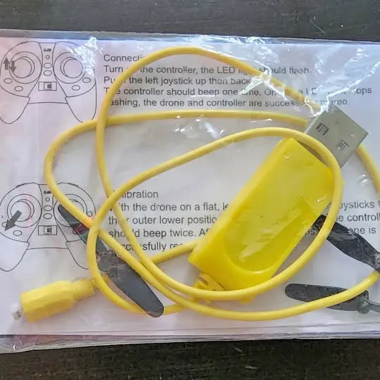 Yellow drone controller with attached cables and instruction sheet background