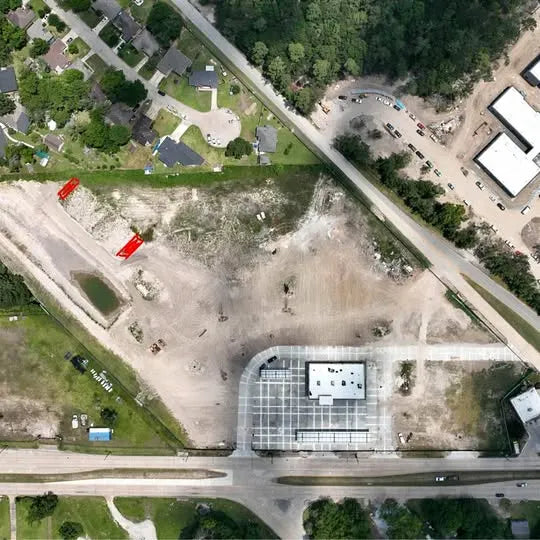 Aerial view of a building and parking lot with surrounding roads and trees