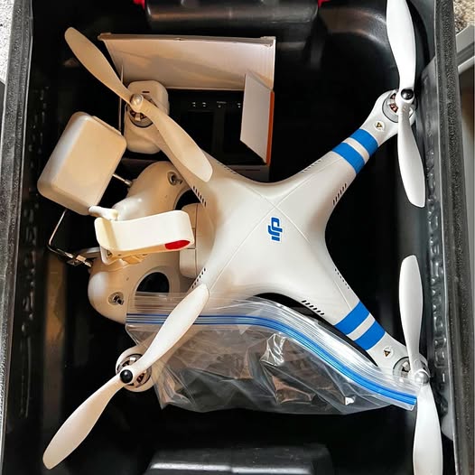 White quadcopter drone with blue stripes, visible propellers and camera mount