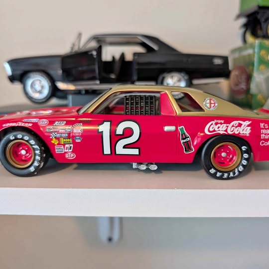 Red diecast racing car with black hood, number 12, Coca-Cola logos.