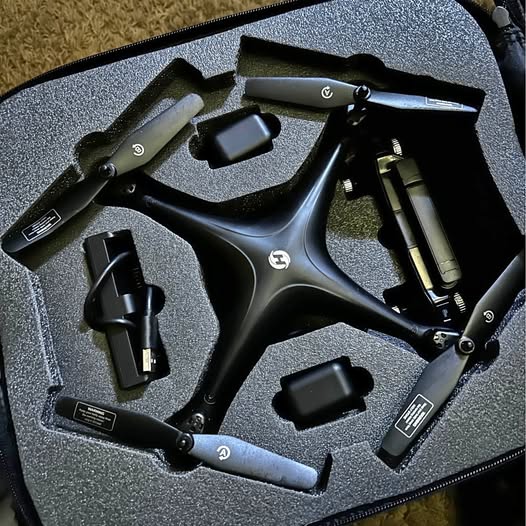 Folded black drone in foam-lined hard case with controller and charging cables