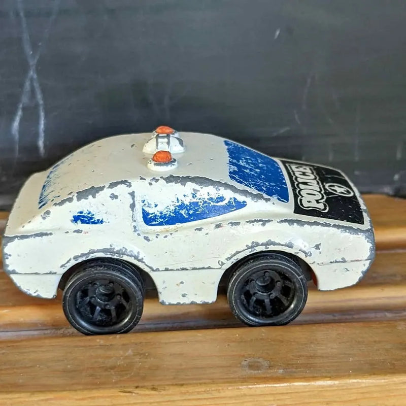 Vintage diecast police car toy with white body, blue stripe, orange light and black wheels