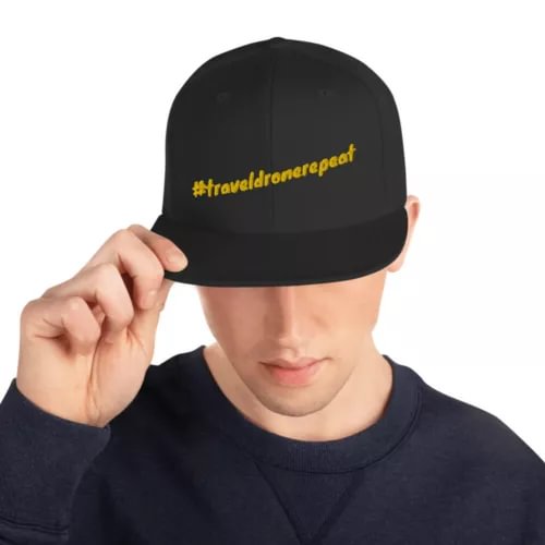 Black snapback hat with yellow #traveldronerepeat logo on front