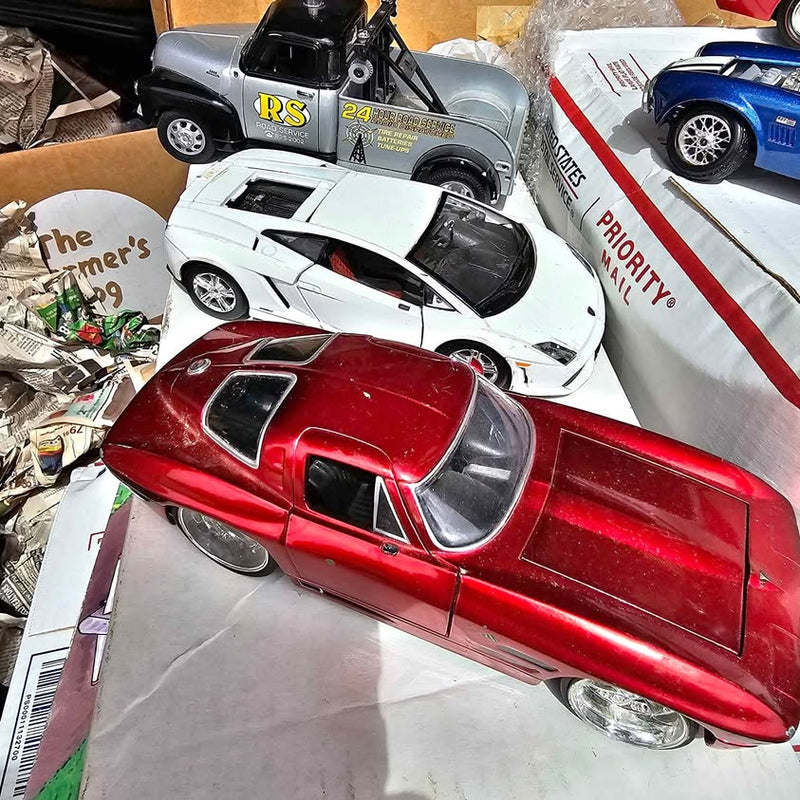 Red diecast sports car model with black windows and silver wheels; white car behind