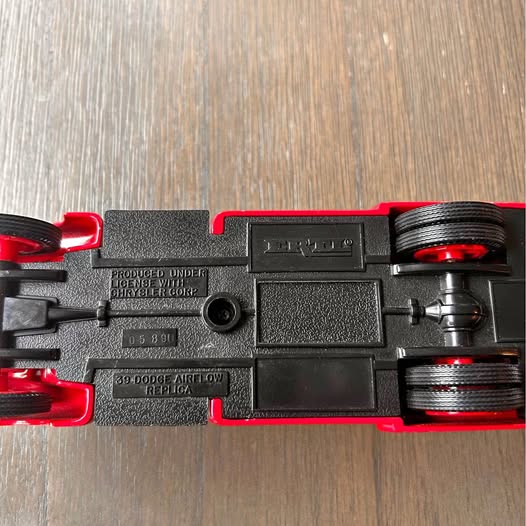 Diecast car chassis with black body and red wheel components, rear and underside view