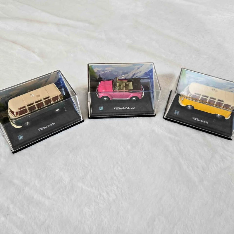 Diecast Volkswagen model cars in display boxes: cream, pink, and yellow bus