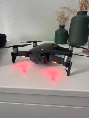 Black quadcopter drone with front camera and spinning propellers, visible status lights