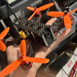 Orange FPV quadcopter drone with four propellers, held in a hand