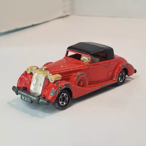 Red diecast roadster car with black roof, chrome grille and bumper, front-left view