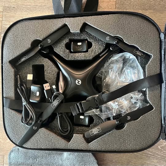 Black drone in hard case with remote, batteries, USB cable, and extra parts