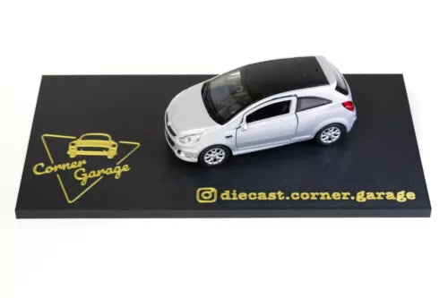 1:34 die-cast model car, silver hatchback with black roof on display base.