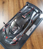 Metallic gray diecast model car with black carbon-fiber base and red accents