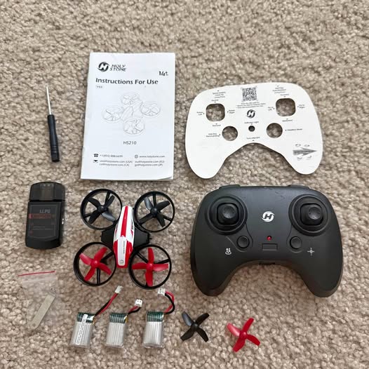 Black drone controller with hand grip, instruction sheet, and multirotor parts
