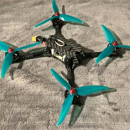 Quadcopter drone with teal four-blade propellers and black carbon-fiber frame