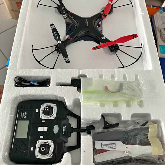 Small drone set with black quadcopter, controller, and spare parts in tray