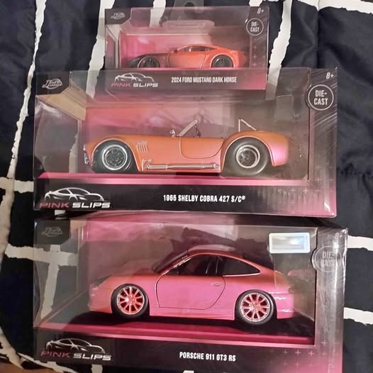 Two boxed diecast model cars: orange road car and light pink sports car
