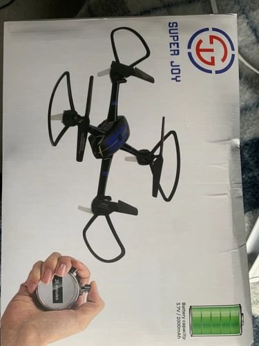 Foldable quadcopter drone on retail box, with hand holding small battery
