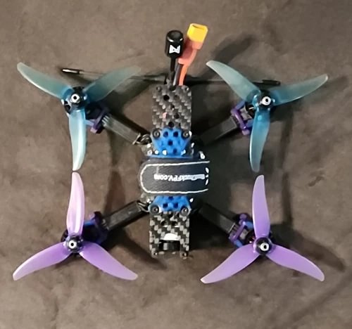FPV quadcopter drone with teal and purple propellers, carbon-fiber body