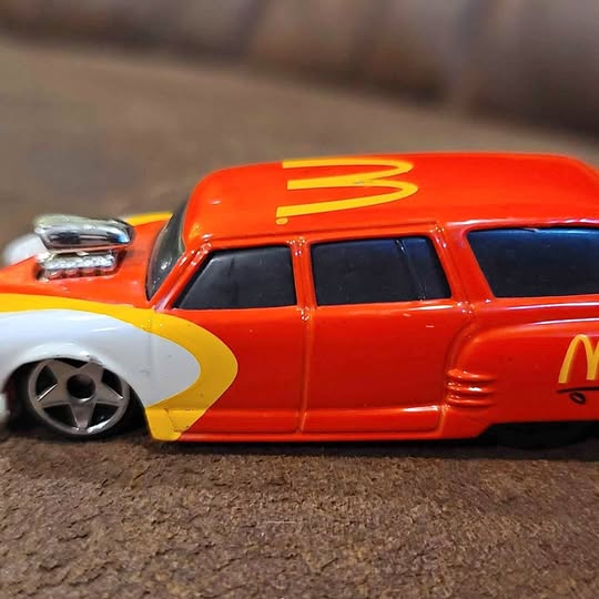 Orange diecast toy car with black windows and white wheels, side view