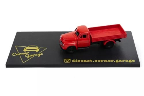 Red die-cast model truck with open cargo bed, on black display base
