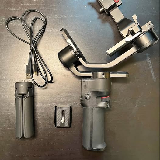 Camera gimbal stabilizer with grip handle and mounting arm, plus USB cables and case