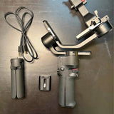 Camera gimbal stabilizer with grip handle and mounting arm, plus USB cables and case