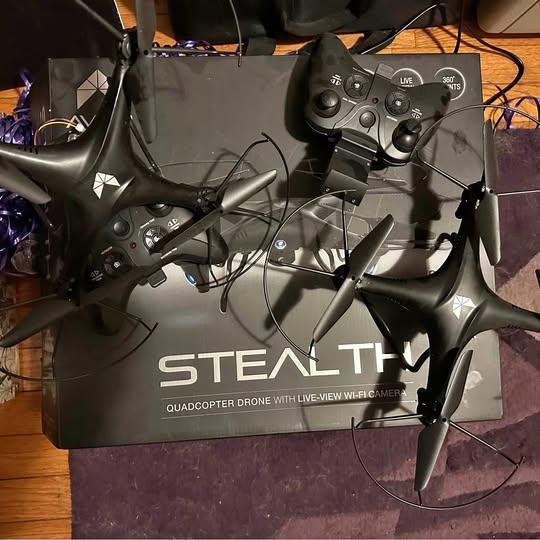 Quadcopter drone with four propellers and dark gray body, with controller