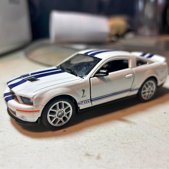 Diecast sports car model, white with blue racing stripes, front 3/4 view