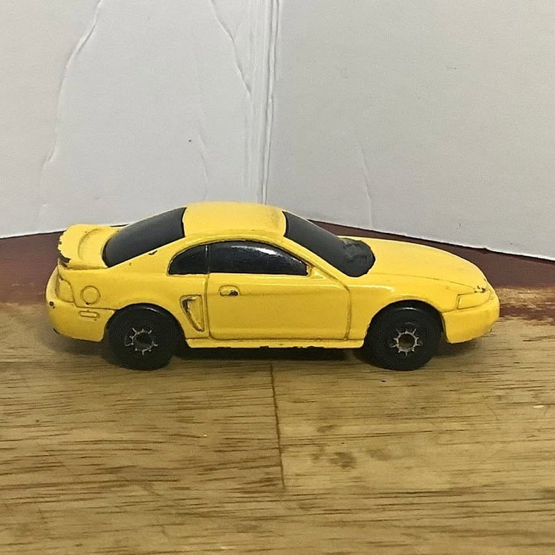 Yellow 1999 Ford Mustang diecast car, 1:64 scale, black wheels, side view