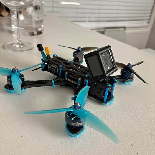 Black FPV racing drone with turquoise prop guards and action camera screen