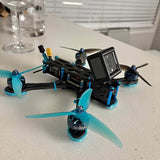 Black FPV racing drone with turquoise prop guards and action camera screen