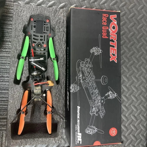 Racing quadcopter drone with green and orange propellers, with product box