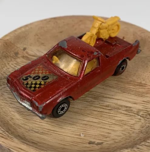 Red diecast pickup truck with open bed and yellow driver figure, detailed front grille