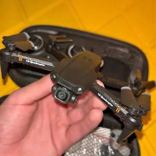 Black quadcopter drone with front camera and prop guards, held in hand