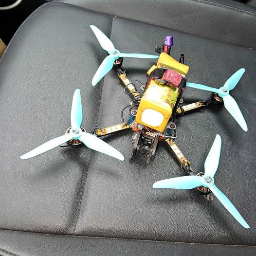 FPV quadcopter drone with four light-blue propellers and yellow control module.