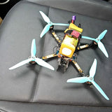FPV quadcopter drone with four light-blue propellers and yellow control module.