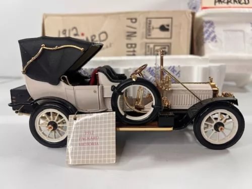 Vintage diecast model car with cream body, dark hood, and gold details